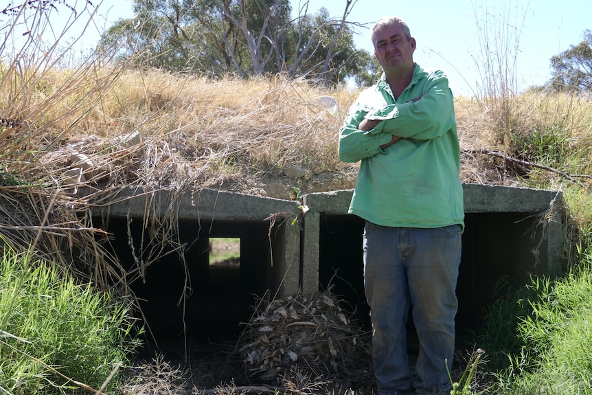 man in green shift stands in front of culvert