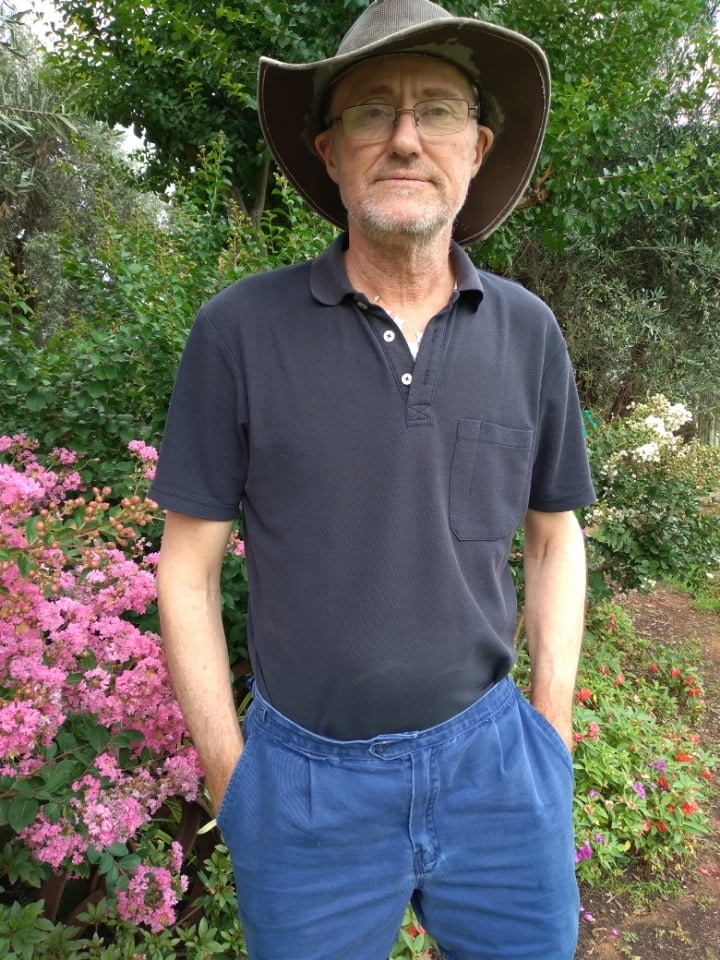 A man stands in front of a flower bed with his hands in his pockets.