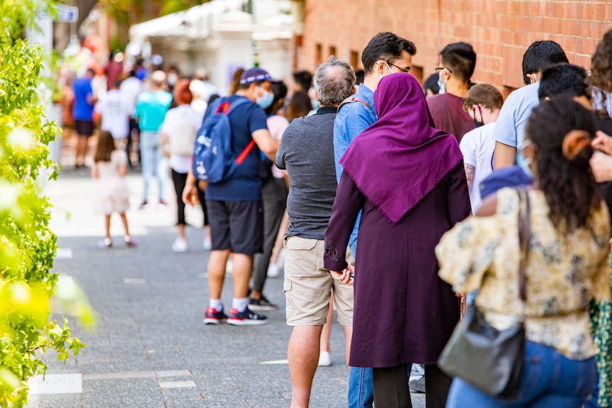 A woman in a purple headscarf waits in a long line.