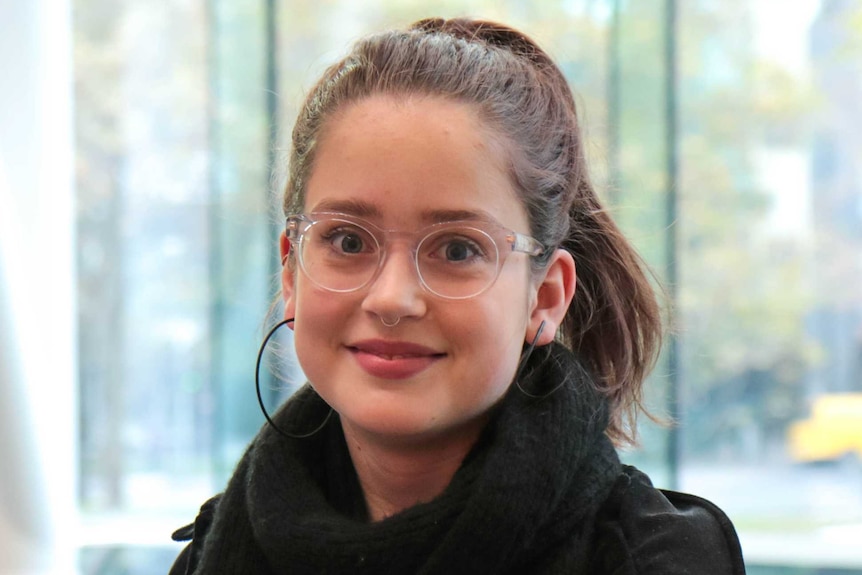 A teenage girl with glasses and a noise ring looks at the camera, smiling.