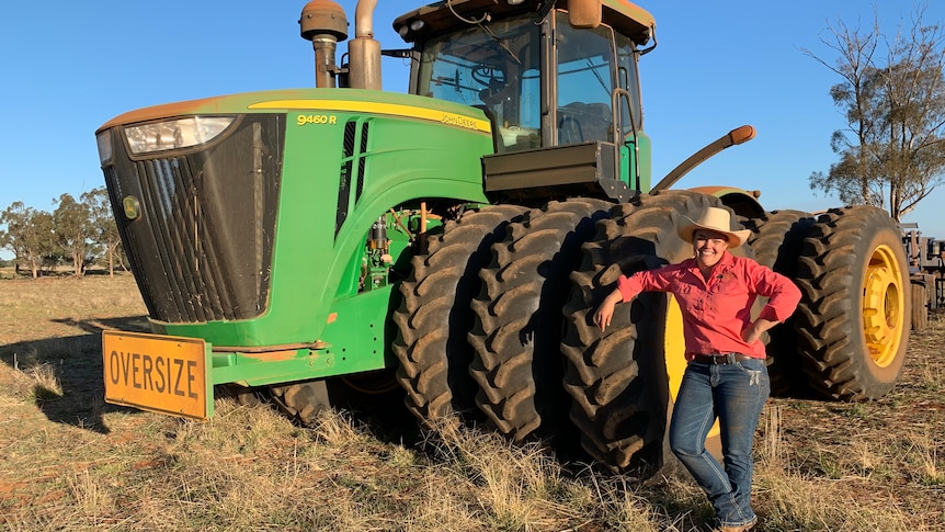 a  woman leaning on the wheel of a very large tractor