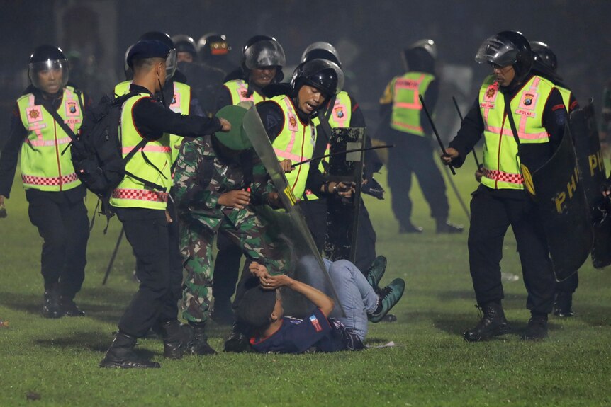 Riot police with batons and shields surround man on ground.