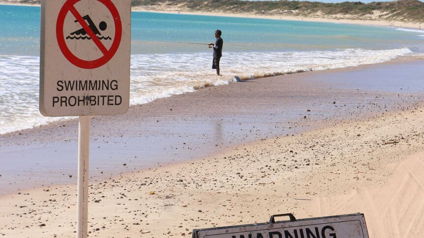 Man fishing next to swimming prohibited sign