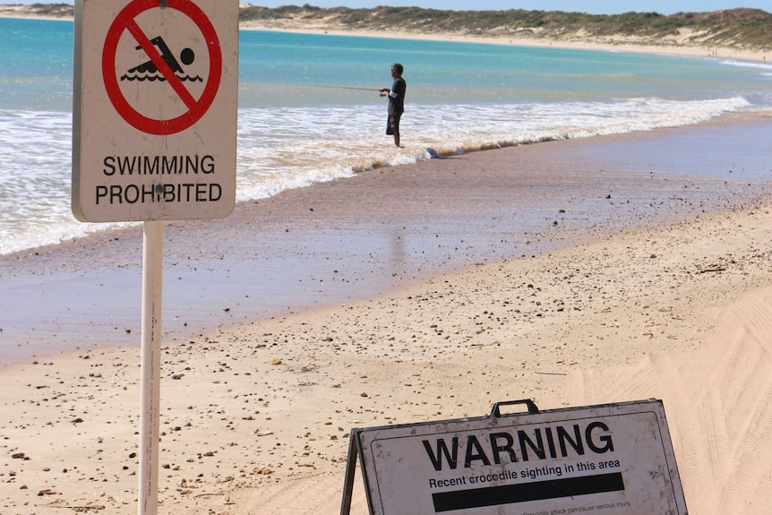 Man fishing next to swimming prohibited sign