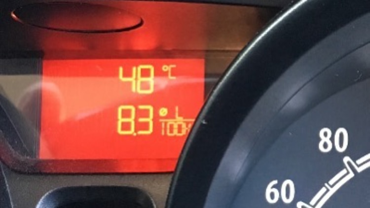 The dashboard of a car shows the temperature outside is 48 degrees Celcius.