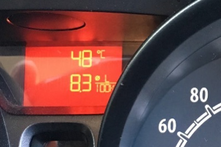 The dashboard of a car shows the temperature outside is 48 degrees Celcius.