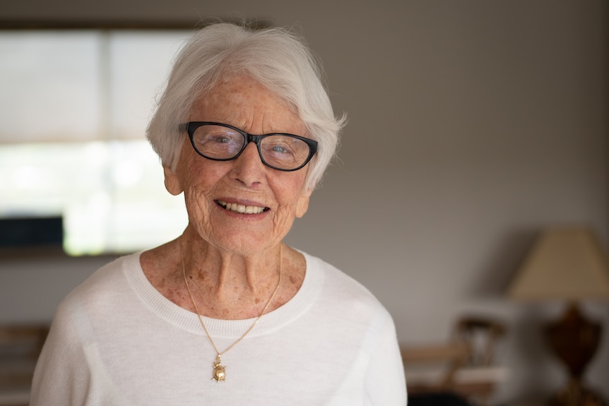 Woman with white hair, black glasses smiling headshot