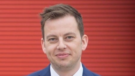 A man wearing a suit and tie standing in front of a red stripy wall