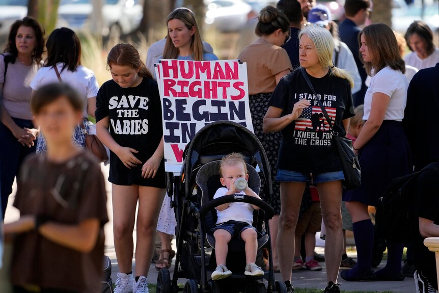 A group women and children stand while holding signs.