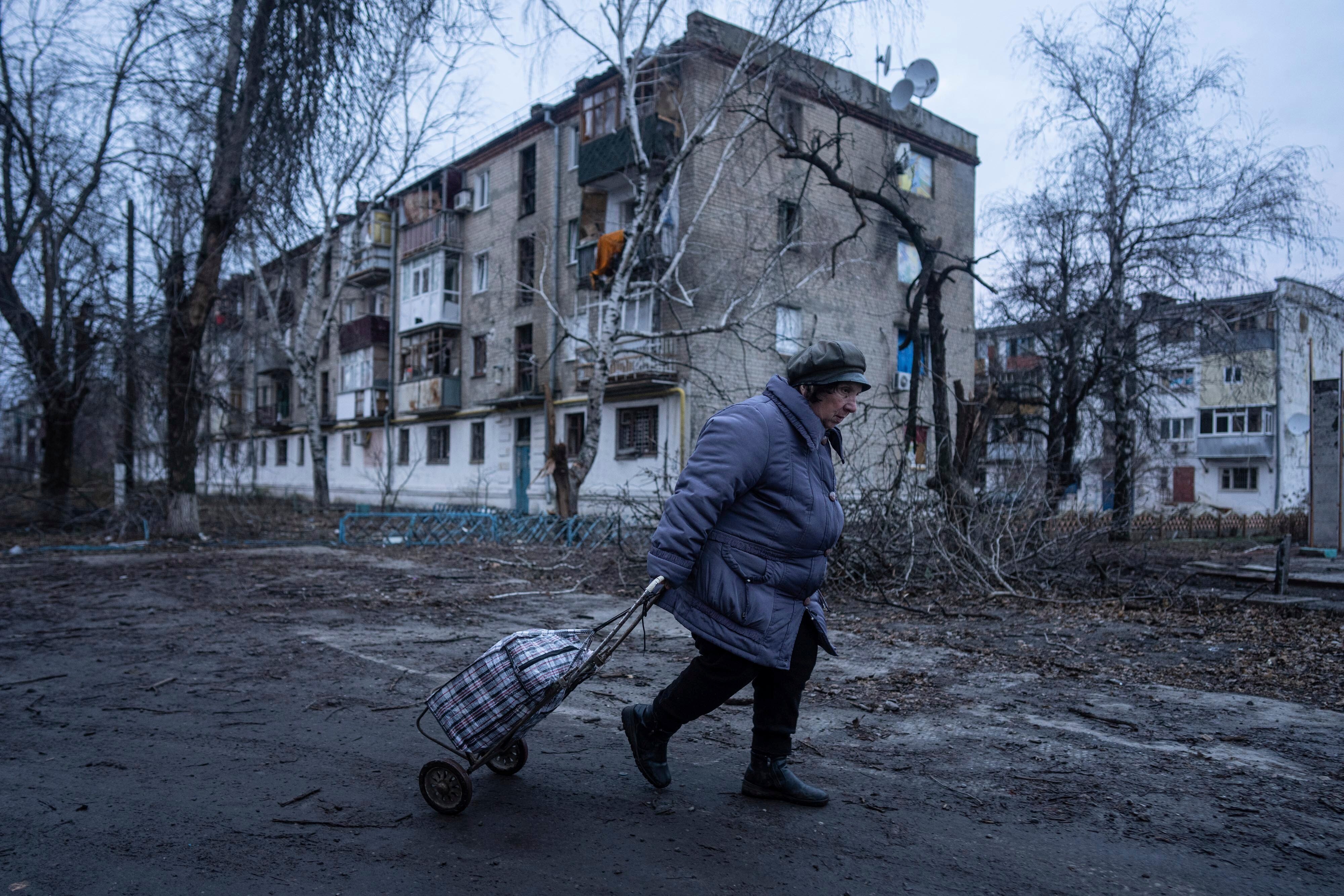 a woman pulls a trolley along a road outside a damaged building in winter