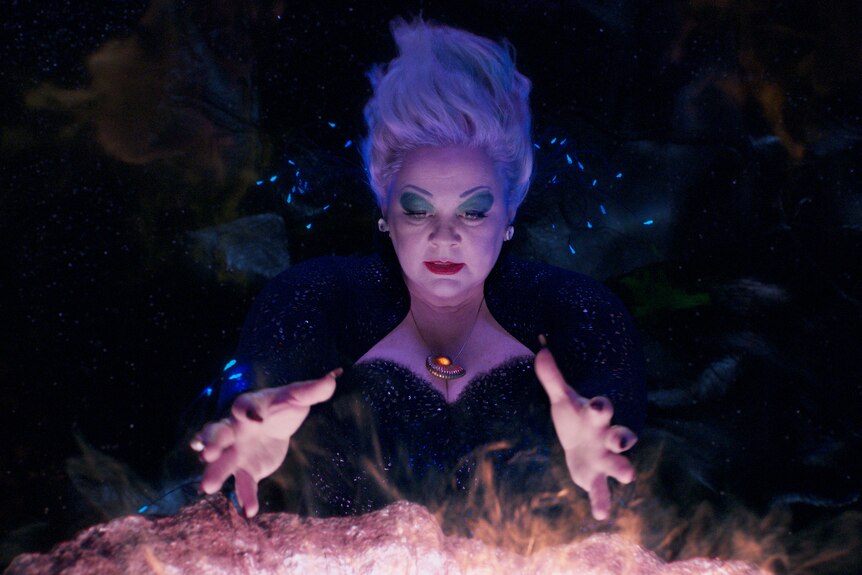 Melissa McCarthy as Ursula in The Little Mermaid. She has short white hair, blue eyeshadow, red lipstick and a black dress.
