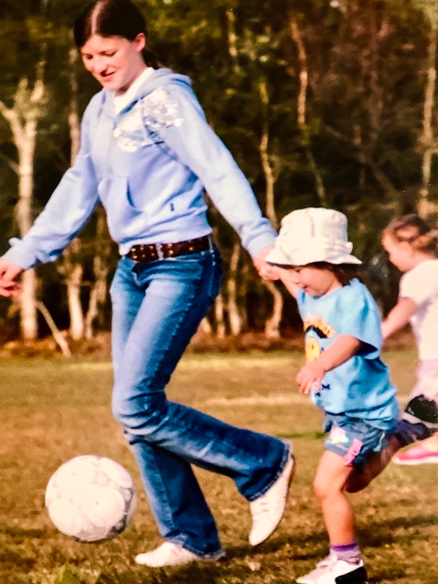 Kyra Cooney-Cross as a young girl holding a woman's hand and running to kick a soccer ball.