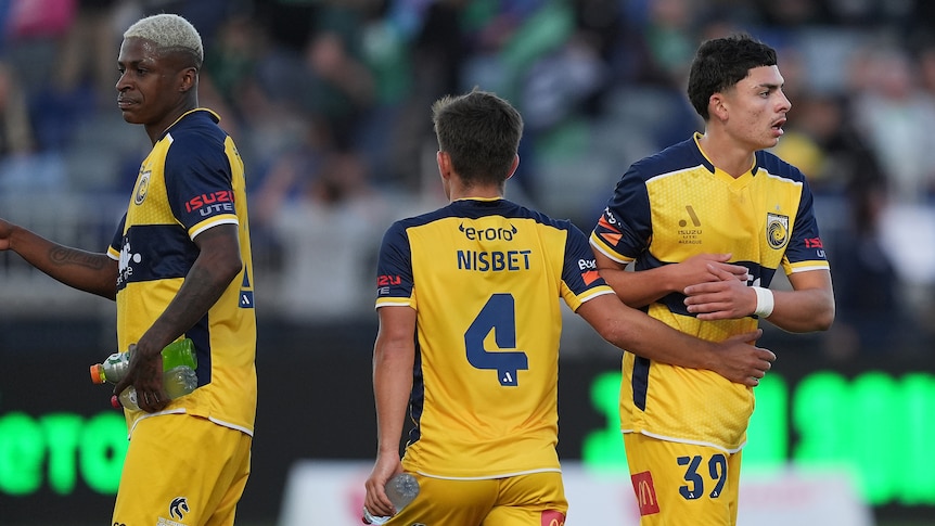 A trio Central Coast Mariners players stand on the ground after winning their ALM match against Western United.