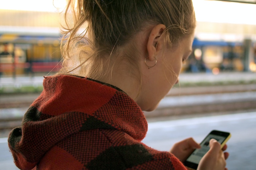 A young woman on a train platform looking at her phone
