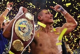 Tim Tszyu holds up his WBO super-welterweight belt and points to the sky as confetti falls around him.