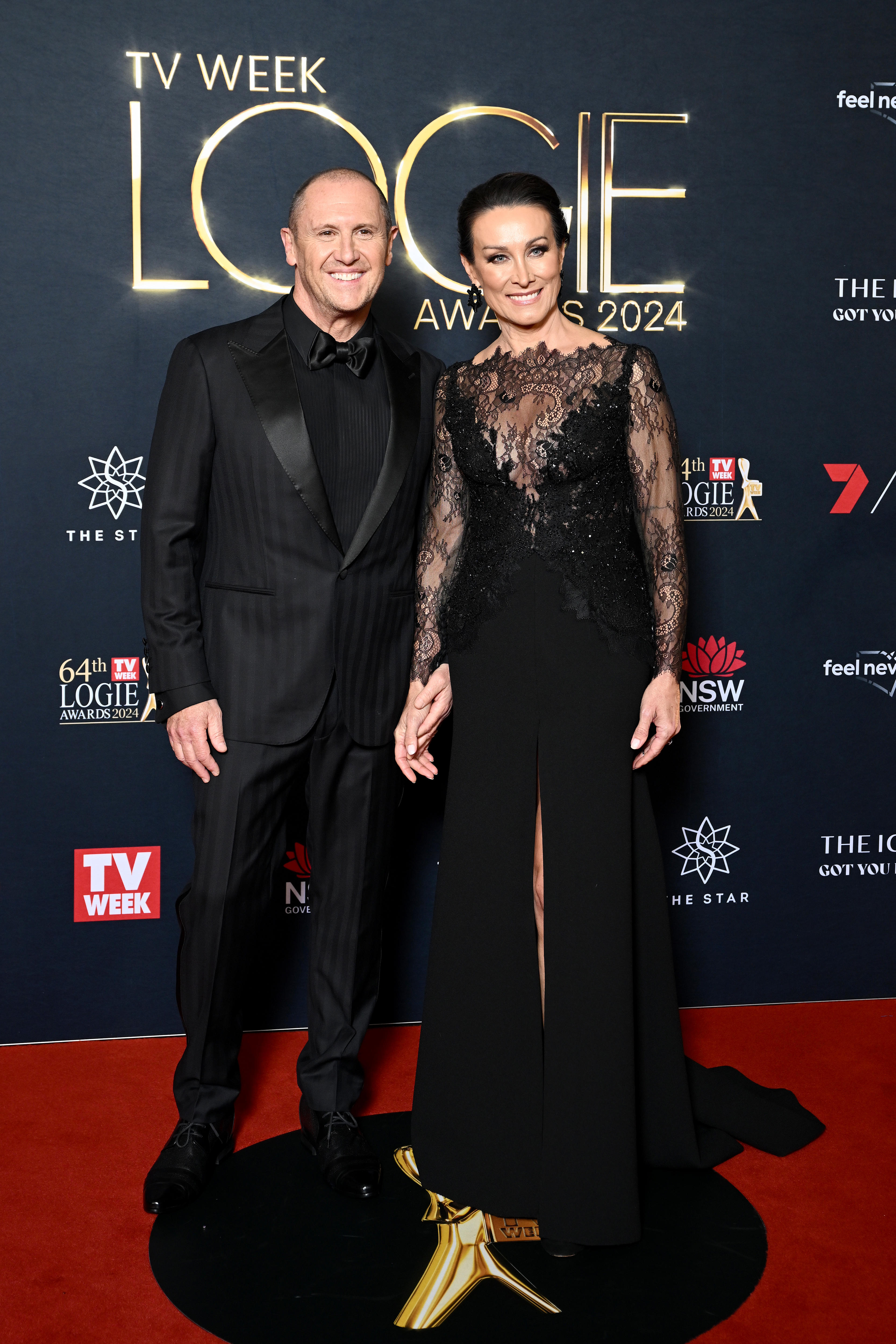 Larry wears a black suit and dress shirt. Sylvie wears a sheer black lace gown