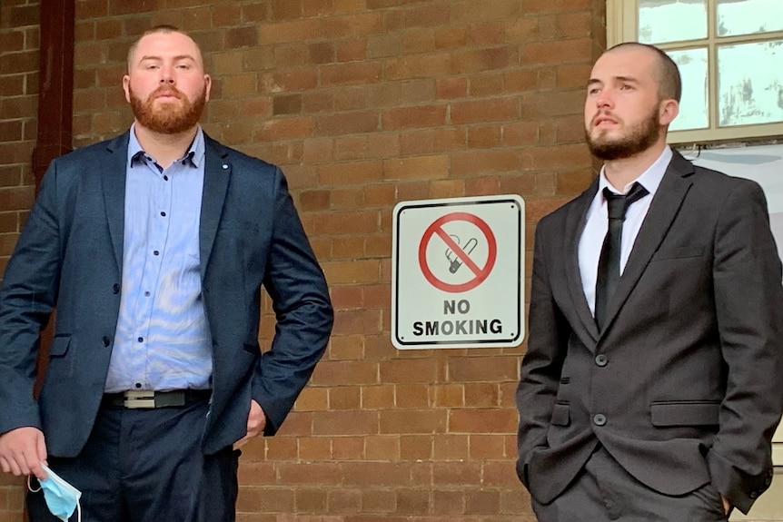 Two men standing a small distance apart on the steps of a court house, looking serious.
