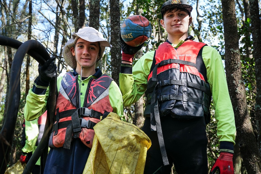 Two teenagers holding rubbish and bags.