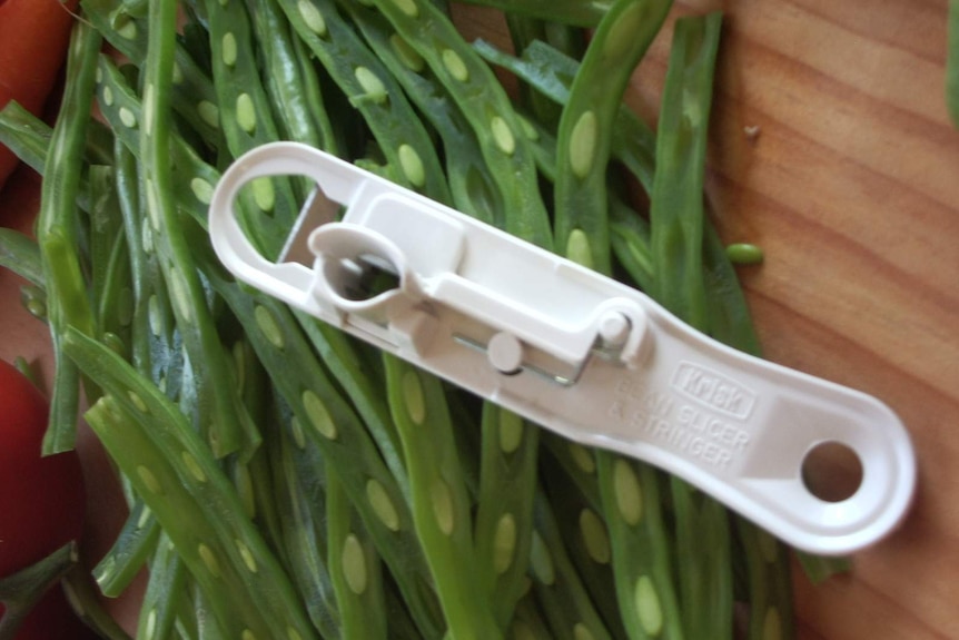 A white plastic Krisk bean slicer sits on a chopping board with sliced beans.