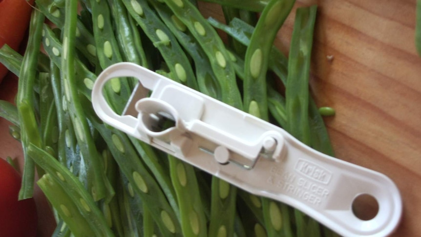 A white plastic Krisk bean slicer sits on a chopping board with sliced beans.