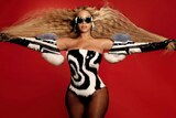 Beyonce wearing a black and white jumsuit with a red background. 