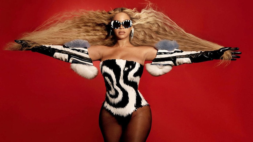 Beyonce wearing a black and white jumsuit with a red background. 