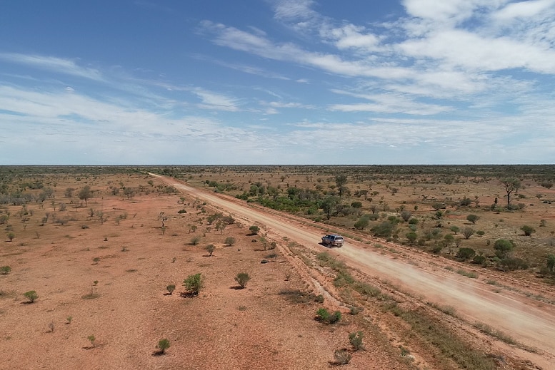 An aerial shot of a silver ute driving on an unsealed road in outback New South Wales.