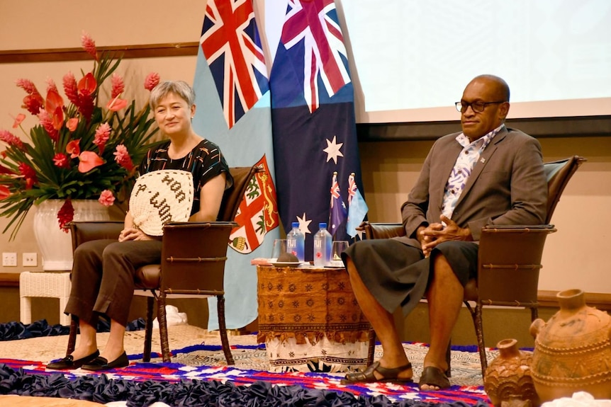 Penny Wong sits on stage behind's Fiji's Minister for Infrastructure and Meteorological Services Jone Usamate.