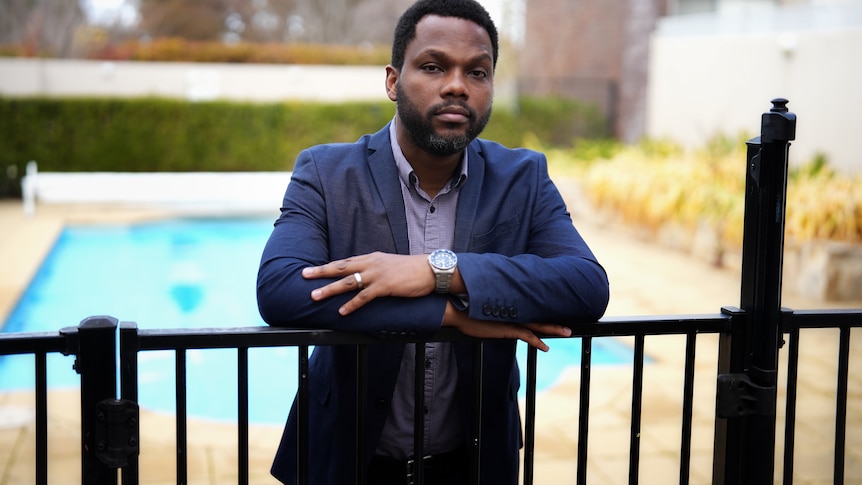 a man of african descent stands behind a pool fence