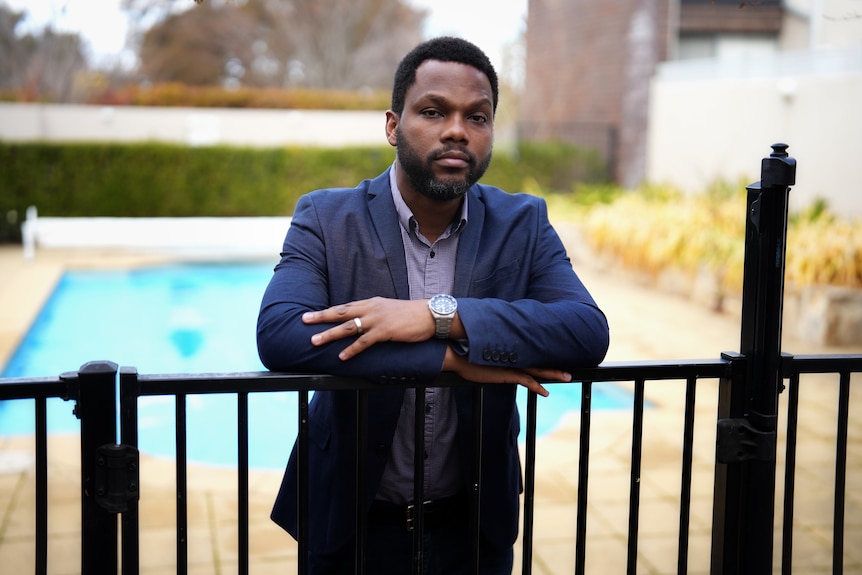 a man of african descent stands behind a pool fence