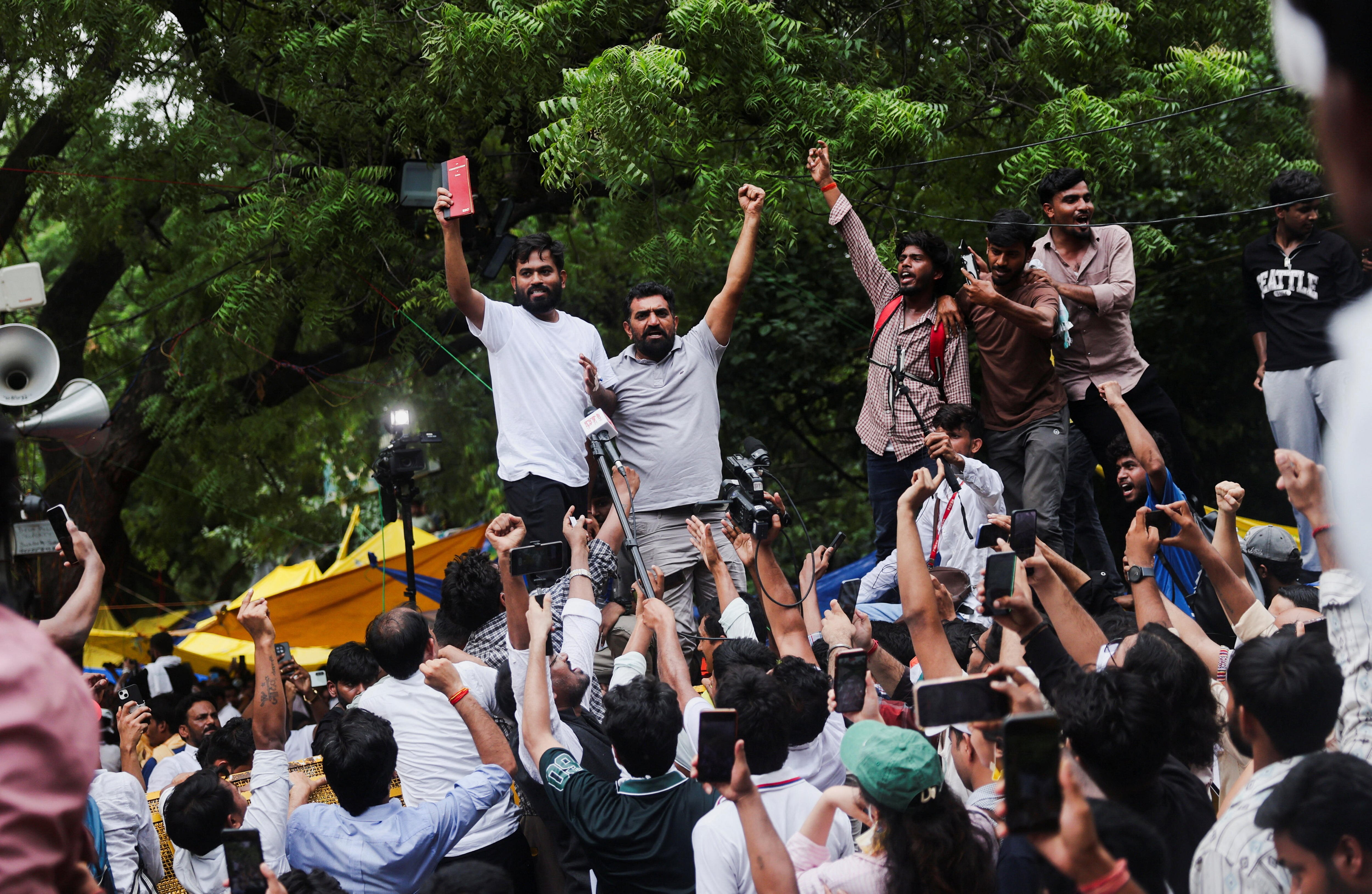 Two men stand on the shoulders of others in a large crowd with their hands in the air as a celebration