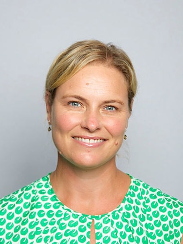A blonde woman wearing a white and green patterned top smiles directly at the camera.