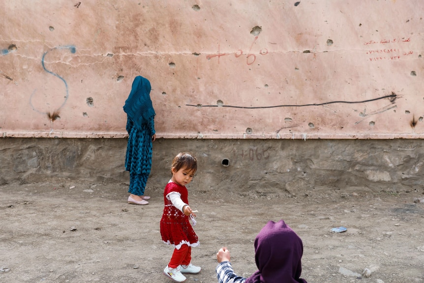 Children stand next to a damaged wall at the site of a car bomb blast that targeted schoolgirls in Kabul