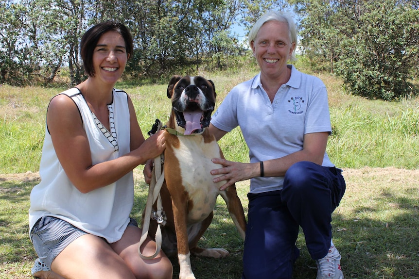 Photograph of boxer and his owner and trainer sitting in the grass, boxer is smiling.