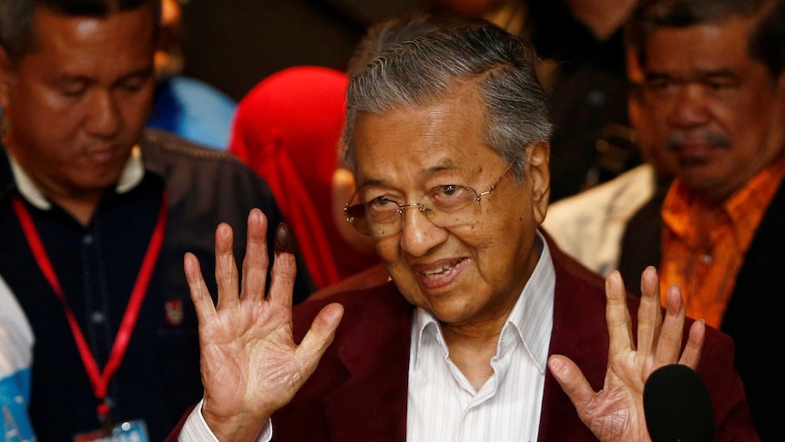 Mahathir Mohamad holds two hands up as he speaks to reporters.