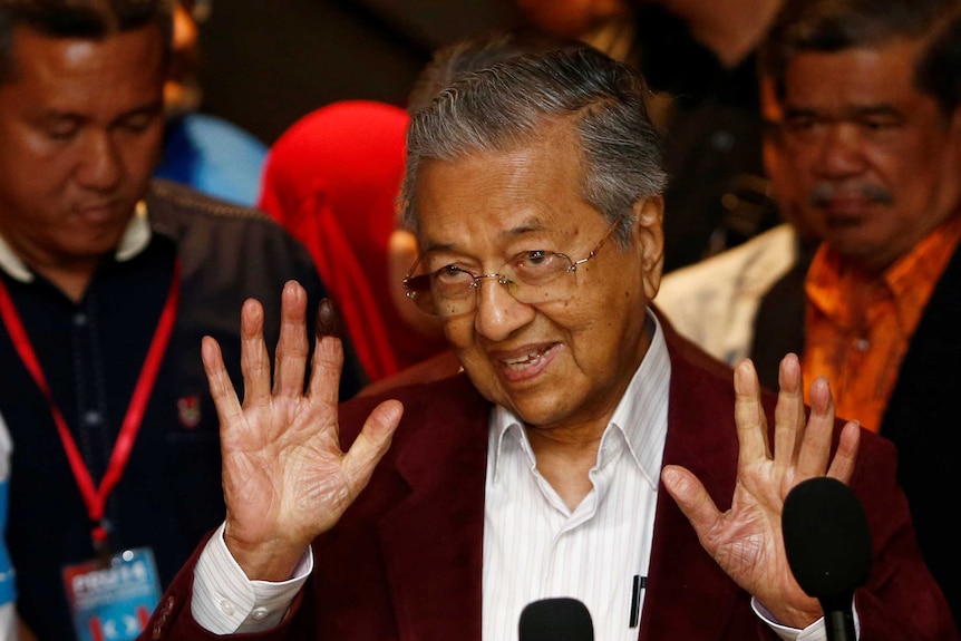 Mahathir Mohamad holds two hands up as he speaks to reporters.