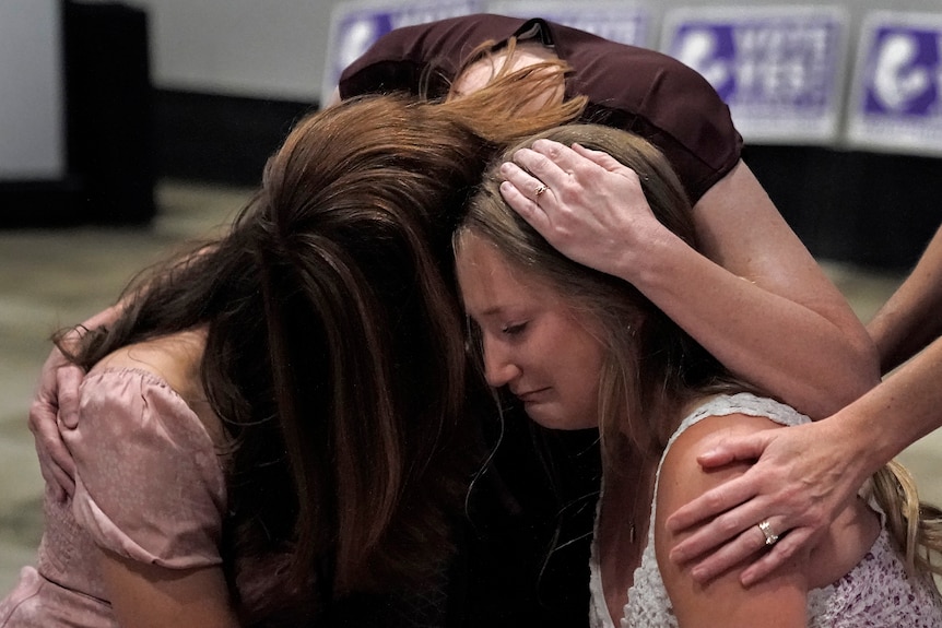Three women push their heads together while crying and embracing