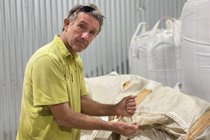 John Lockhart stands next to storage bags filled with stockfeed, stockfeed is also visible in his hands