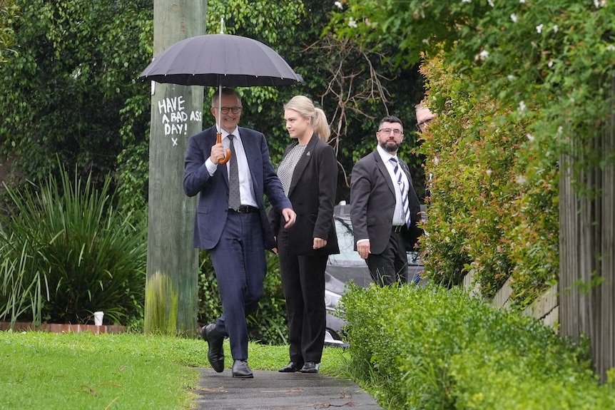 Anthony Albanese walks whilst holding an umbrella