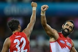Two players in Sydney Swans red and white guernseys fist bump in celebration.