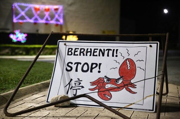 A small sign sitting on a footpath saying 'Stop!' and warning motorists about red crabs with a drawing of a red crab on it.