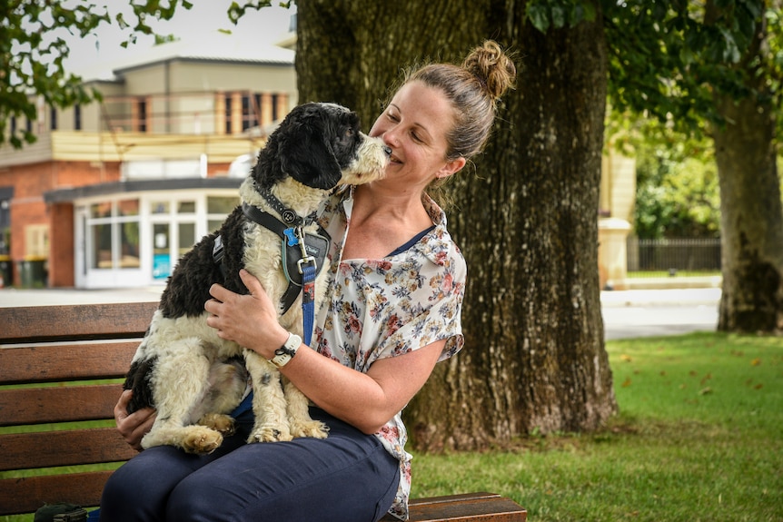 A woman holds a small black and white dog while sitting on a park bench.