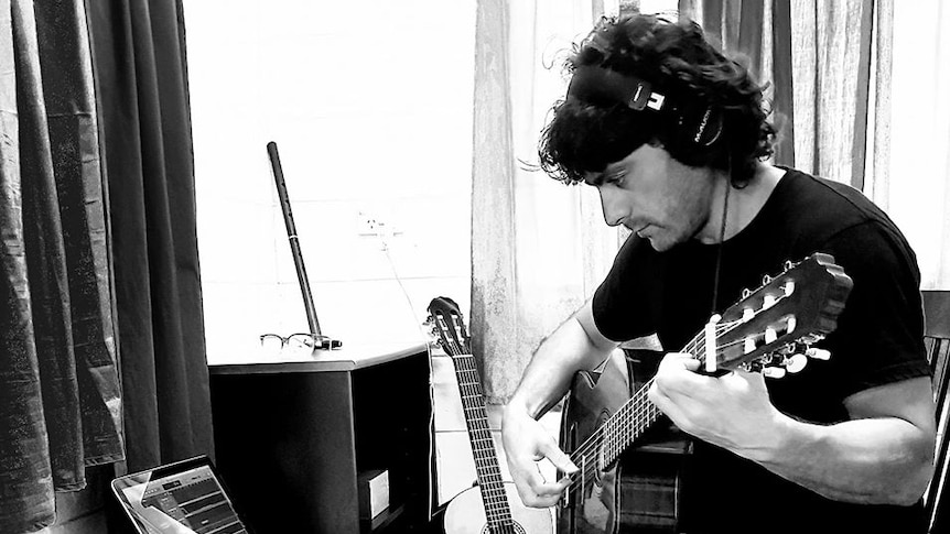 Farhad Bandesh pictured in black and white playing guitar near recording equipment