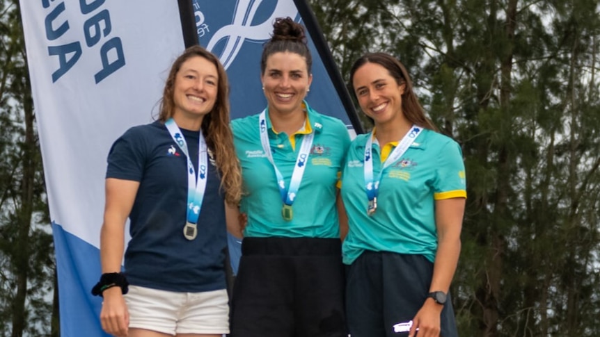 Three women, including Jess and Noemie Fox, stand on a podium with medals around their necks.