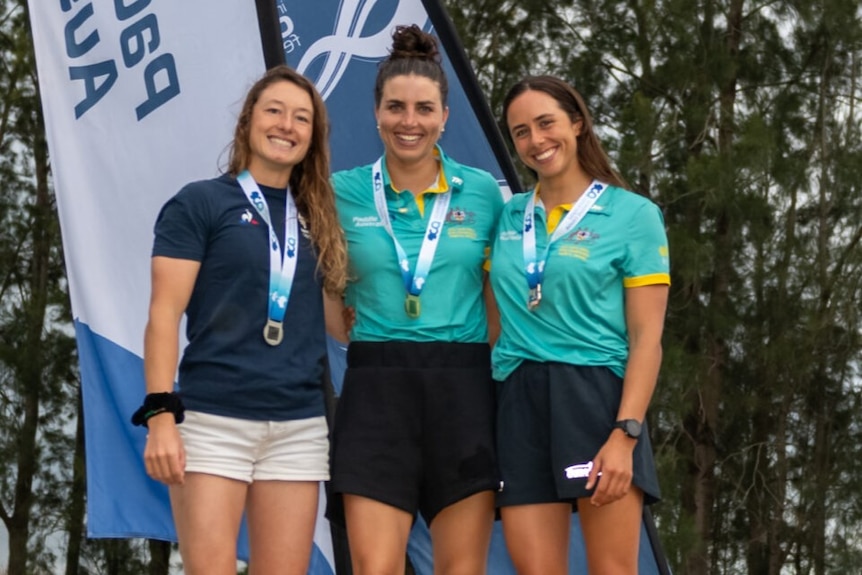 Three women, including Jess and Noemie Fox, stand on a podium with medals around their necks.