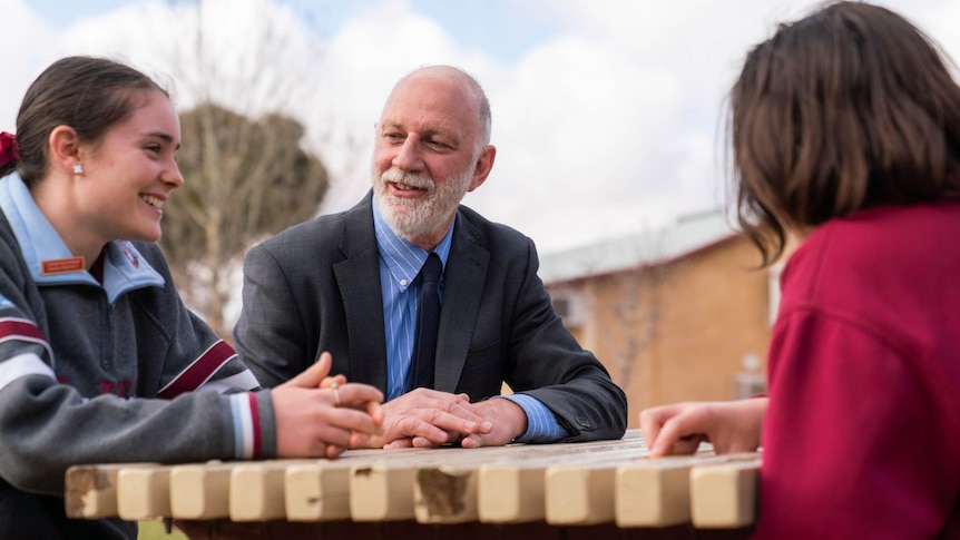 Man sits at a bench talking to a female and male student. 