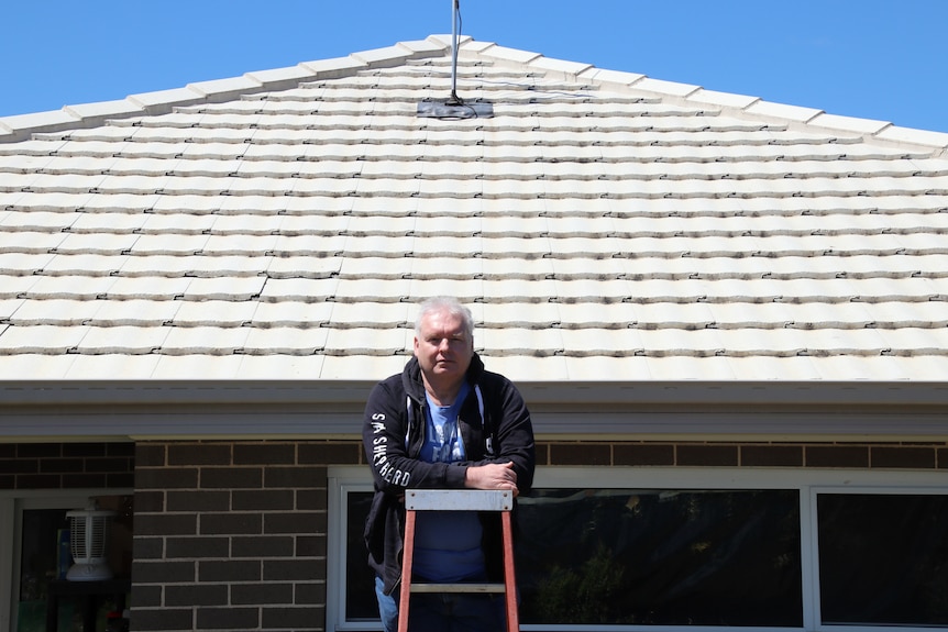 Man standing on ladder in front of white roof.