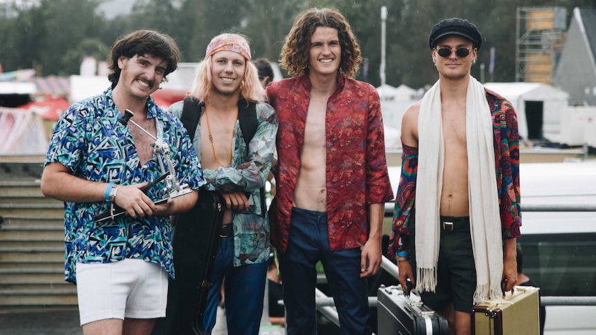 Four men in unbuttoned patterned shirts stand in the rain