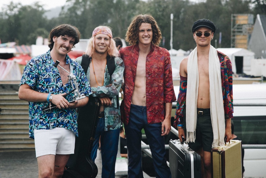 Four men in unbuttoned patterned shirts stand in the rain