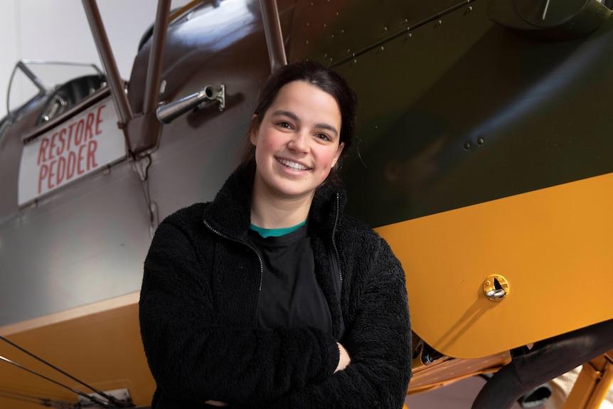 Young woman standing in front of a Tiger Moth plane with a 'Restore Pedder' sign.